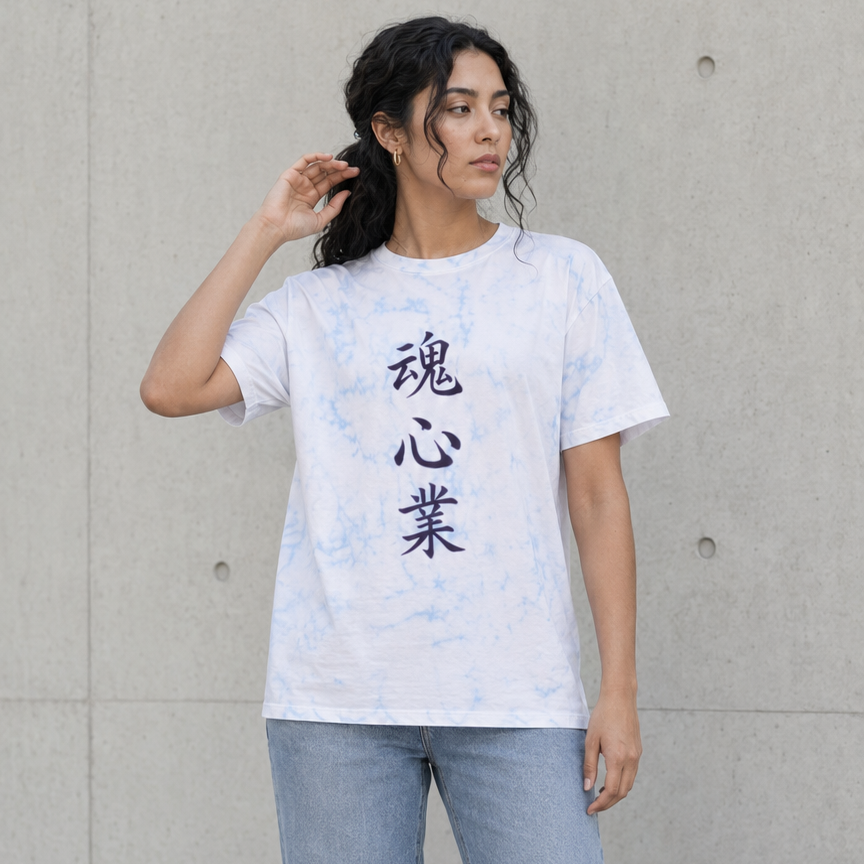 A woman wearing a white short-sleeve t-shirt with black Japanese calligraphy characters on the front, paired with light blue wide-leg jeans and black boots, standing against a concrete wall.
