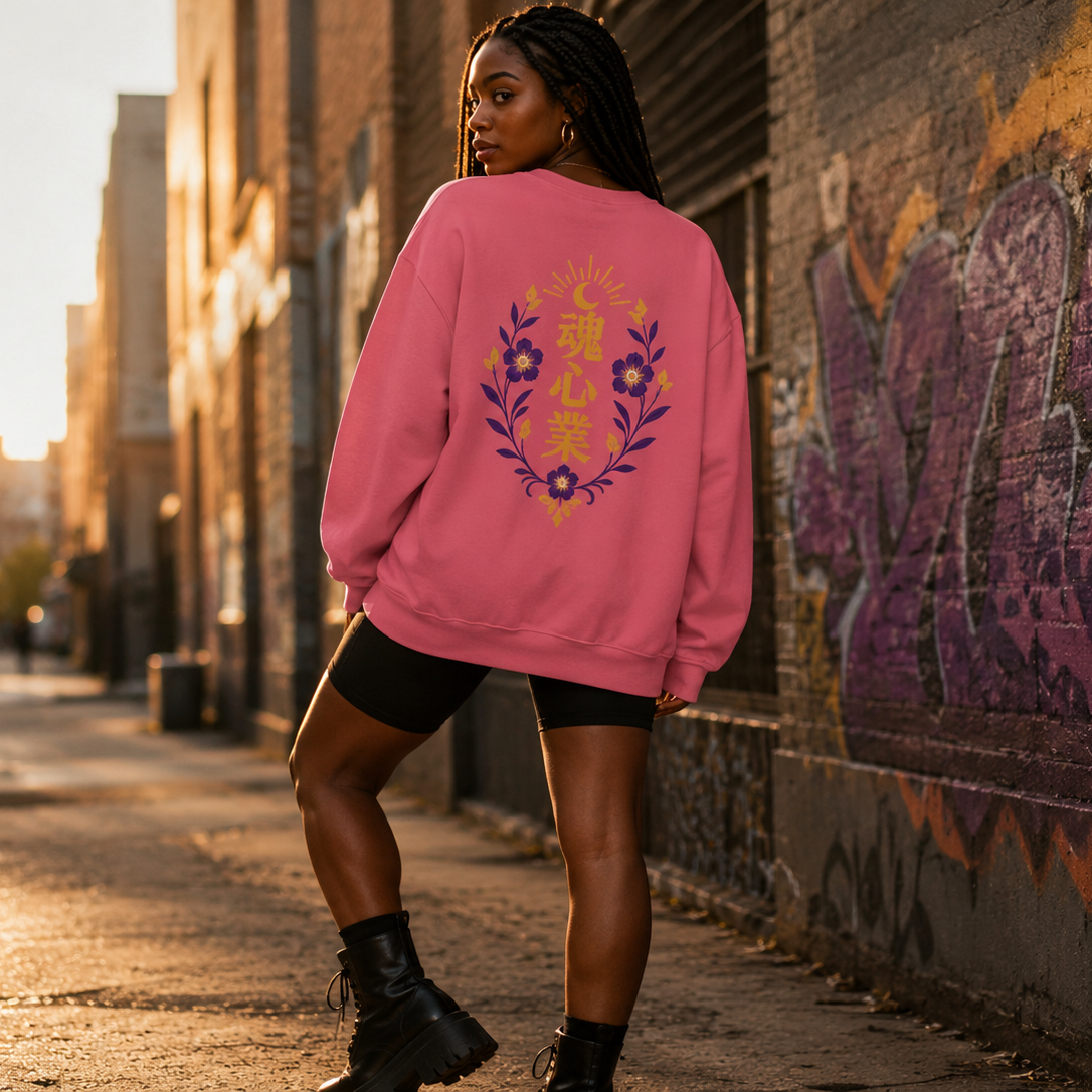Black woman wearing an oversized pink crewneck sweatshirt with a gold and purple Japanese kanji floral crest on the back, styled with biker shorts and platform boots in an urban alley.