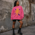 Black woman wearing an oversized pink crewneck sweatshirt with a bold gold and purple Japanese kanji design, styled with biker shorts and platform boots.