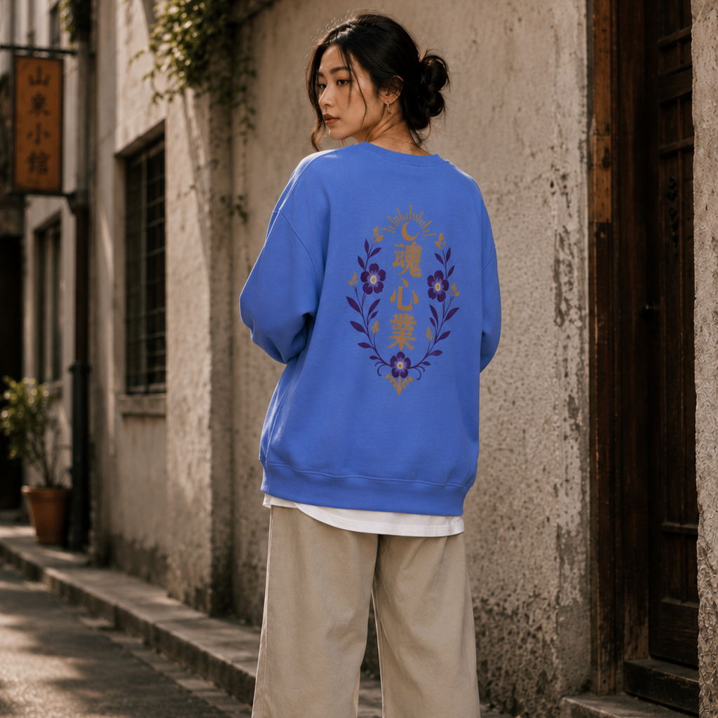 East Asian woman wearing a blue oversized crewneck with a gold and purple Japanese kanji floral crest on the back in an urban alley.