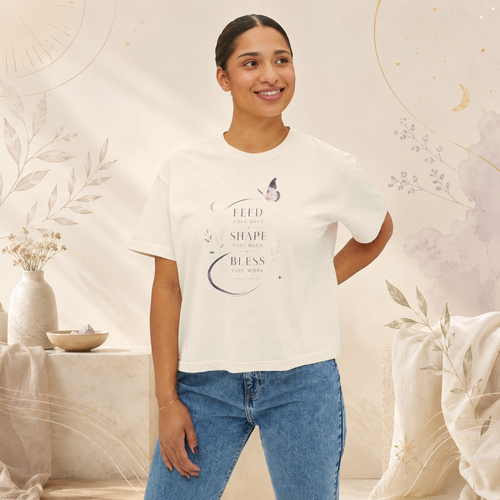 Woman wearing an ivory Soul & Hands boxy T-shirt with a butterfly and Feed, Shape, Bless front graphic.