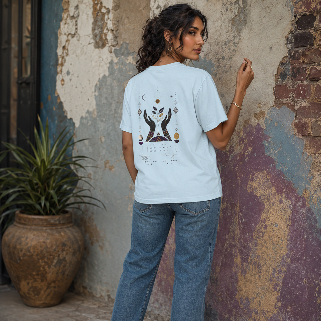 Back view of a woman wearing a light blue Soul & Hands T-shirt with a large hands, botanical and celestial design.