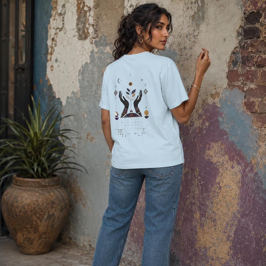 Back view of a woman wearing a light blue Soul & Hands T-shirt with a large hands, botanical and celestial design.