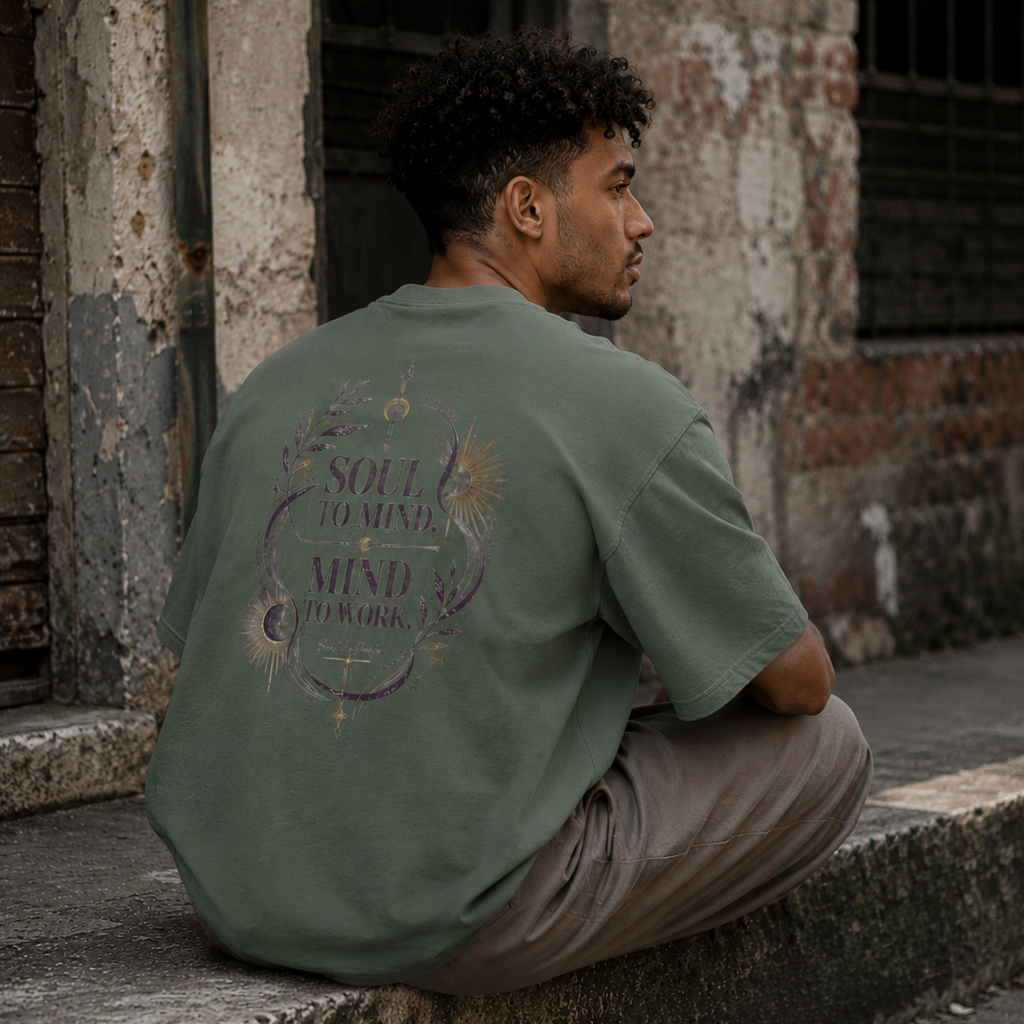 Man wearing a sage green Soul & Hands oversized T-shirt with purple-and-gold Soul to Mind, Mind to Work celestial artwork.