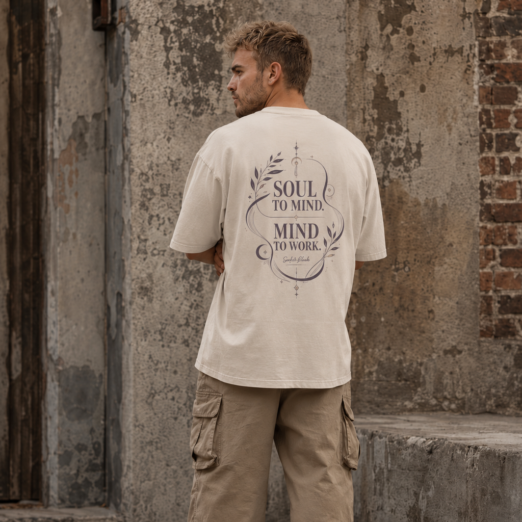 Back view of a man wearing a sand Soul & Hands oversized T-shirt with purple Soul to Mind, Mind to Work botanical artwork.