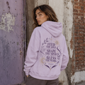Back view of a lavender Soul & Hands hoodie with purple-and-gold Feed the Soul botanical and celestial artwork.