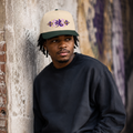 Man wearing a cream Soul & Hands cap with a dark green brim and purple-and-gold kanji soul graphic.