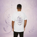 Back view of a man wearing a white Soul & Hands T-shirt with purple-and-gold Feed the Soul, Shape the Mind, Bless the Work artwork.