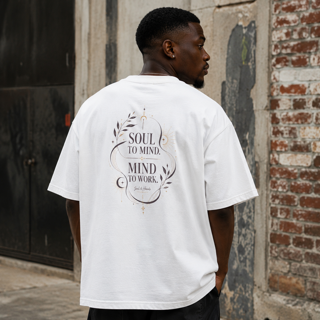 Back view of a man wearing a white Soul & Hands oversized T-shirt with black-and-gold Soul to Mind, Mind to Work botanical artwork.