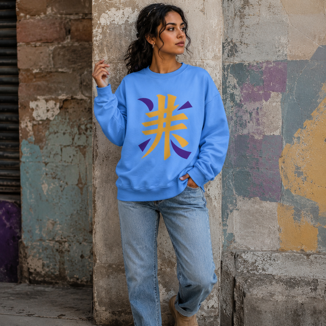 Woman wearing a blue oversized crewneck sweatshirt with a bold gold and purple Japanese kanji design, styled with light-wash jeans in an urban setting.
